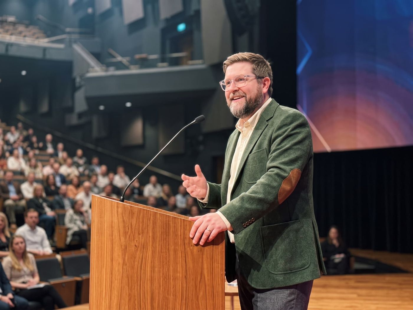 Tanner O. Campbell delivering a keynote from a lectern to a full auditorium
